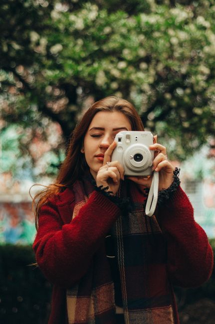 Young woman in red sweater using instant camera outdoors during fall.