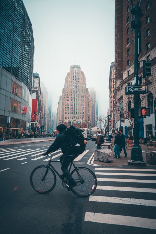 Free A cyclist navigates a foggy downtown New York City crosswalk, capturing urban life and architecture. Stock Photo
