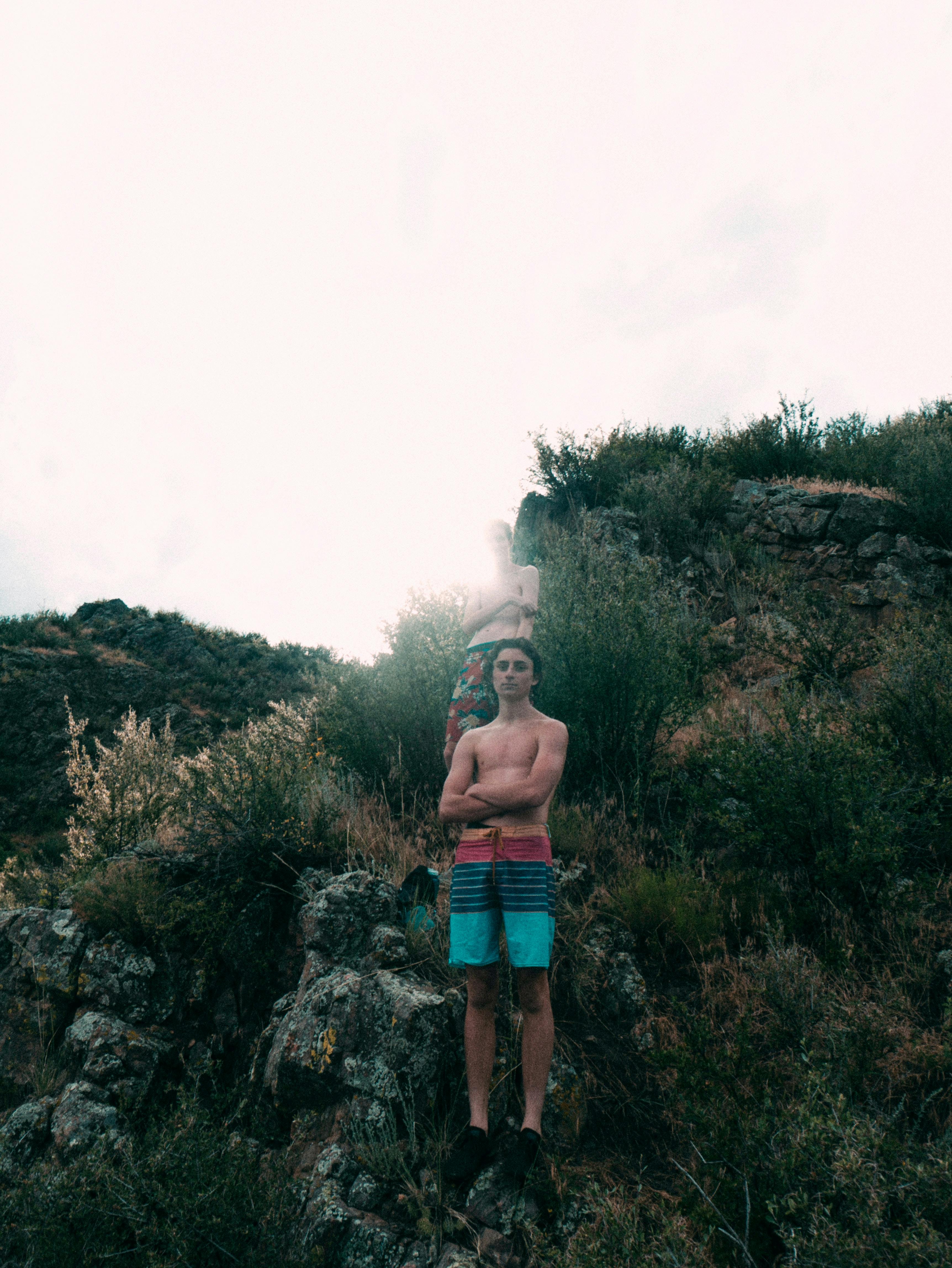 Two shirtless men standing on a rocky cliff with vegetation in Fort Collins, CO.