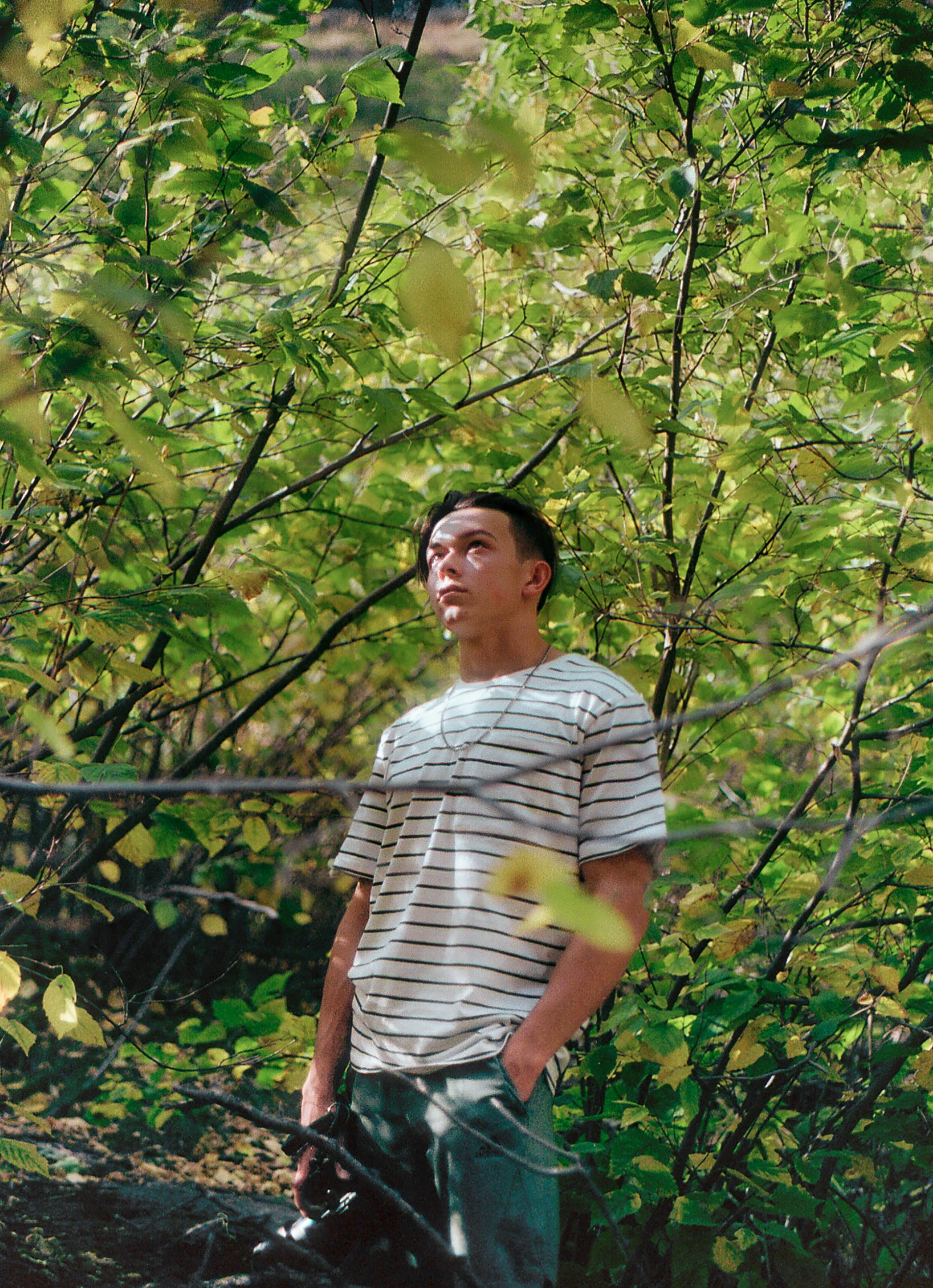 Adult man in striped shirt explores lush green forest in Boulder, CO, capturing nature with a camera.