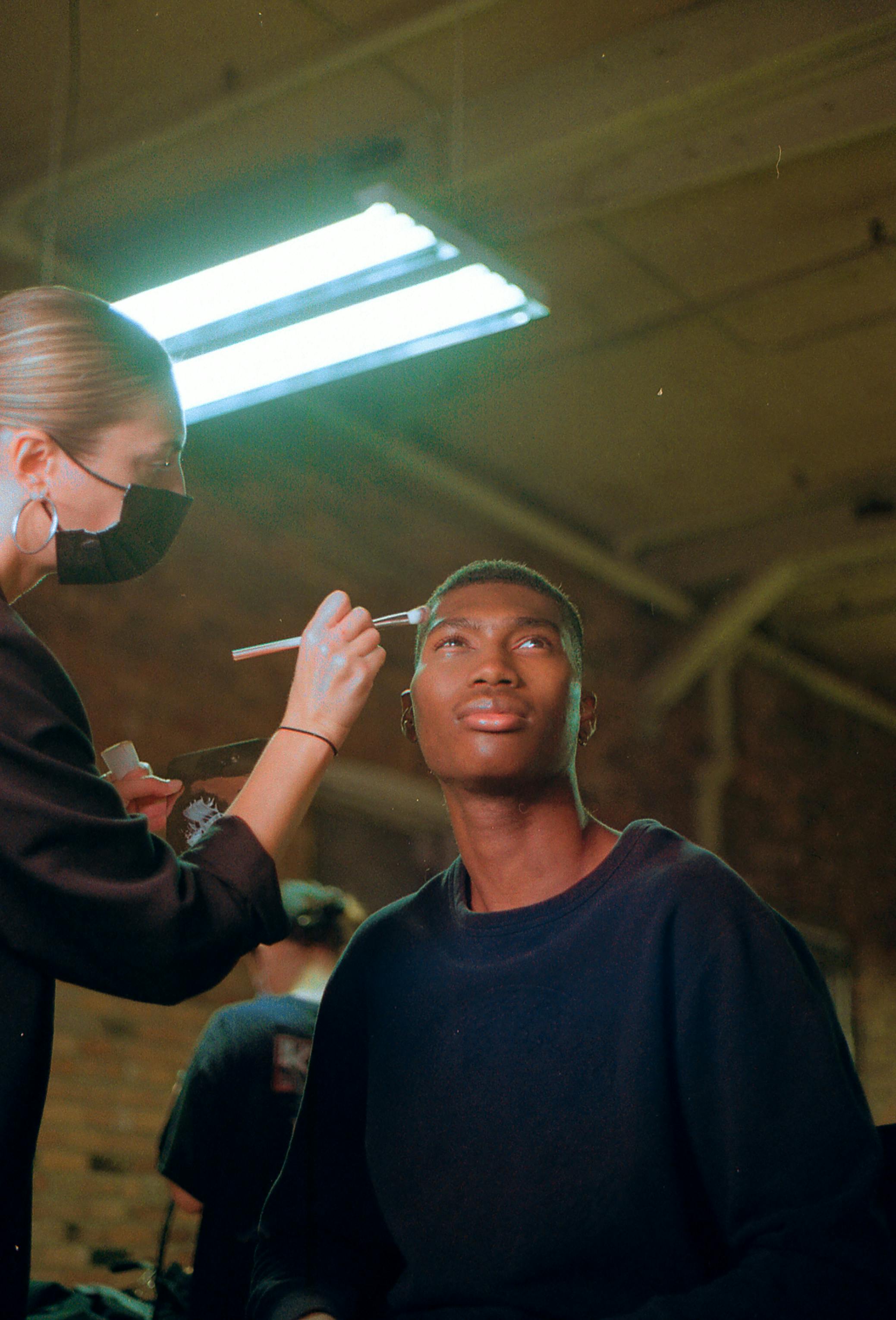 Makeup artist applies cosmetics to a young model during a photoshoot in an urban studio setting.