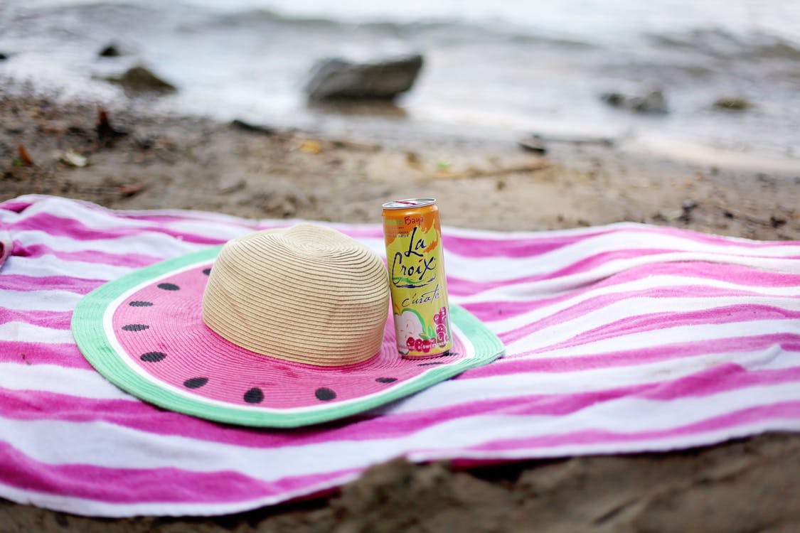 밀짚 모자와 주스 캔으로 모래 해변에 펼쳐진 스트라이프 타월