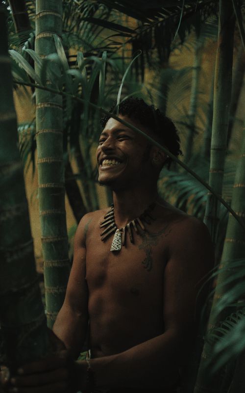 Free A joyful man stands shirtless, surrounded by bamboo in a natural setting, smiling warmly. Stock Photo