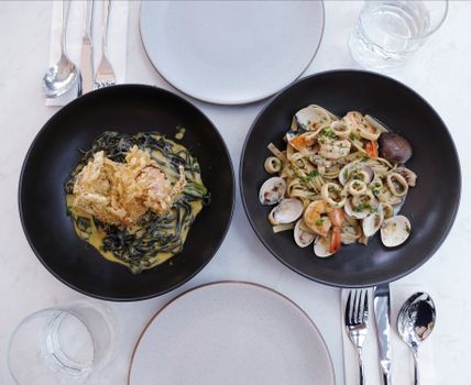 Top view of seafood pasta and tempura dish in black bowls, perfect for dining themes.