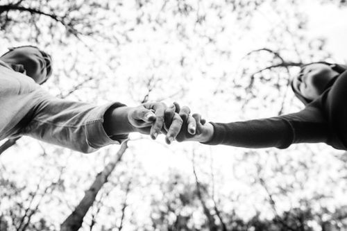 Free A couple holding hands from a low-angle perspective, symbolizing connection against a leafy sky. Stock Photo