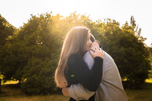 A couple shares a warm embrace under the bright sun in a peaceful park setting.