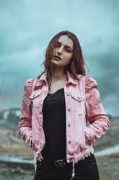 A woman in a pink jacket stands confidently in the rain, exuding a powerful presence.