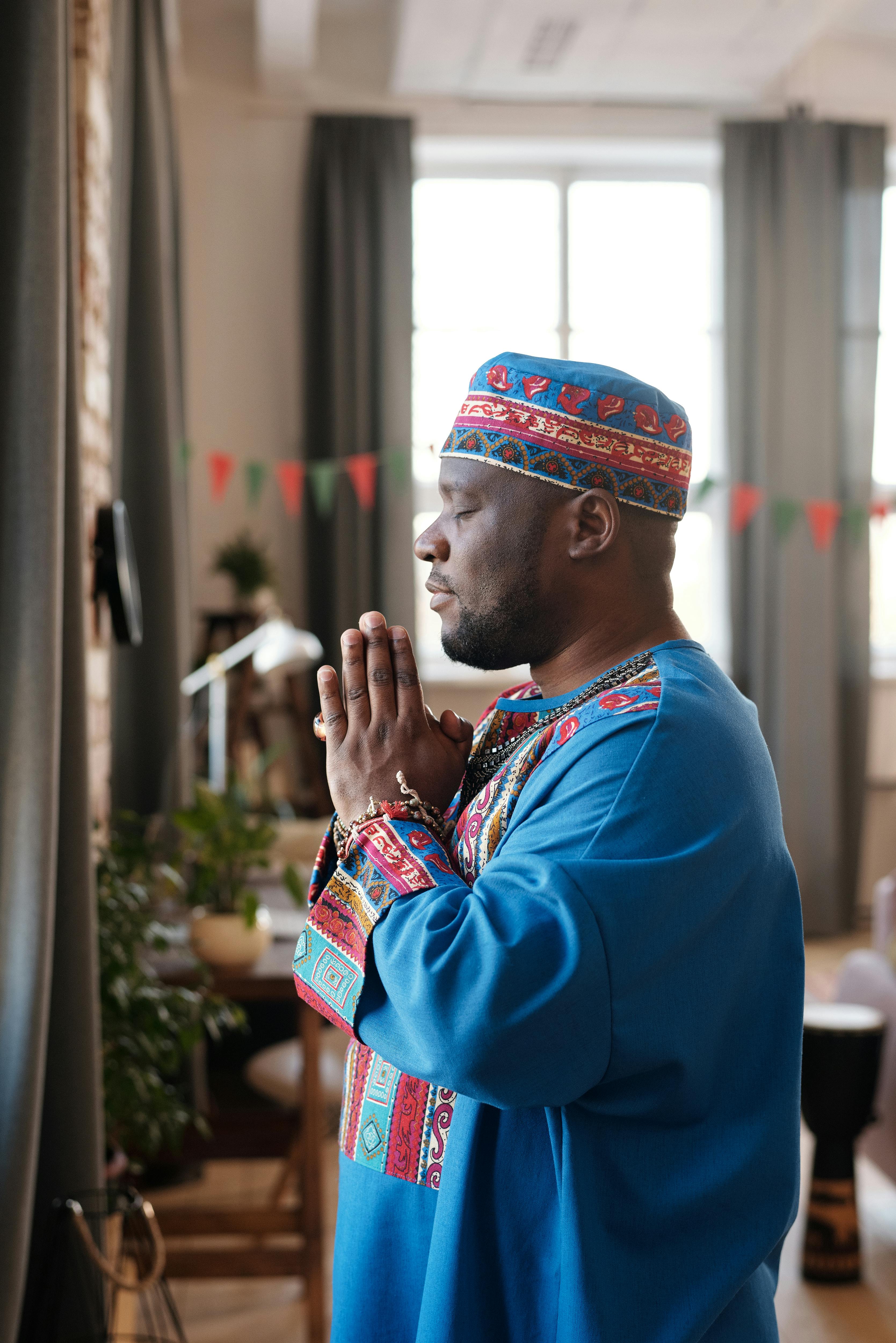 Side view of an African man praying in traditional dashiki indoors, symbolizing cultural heritage and spirituality.