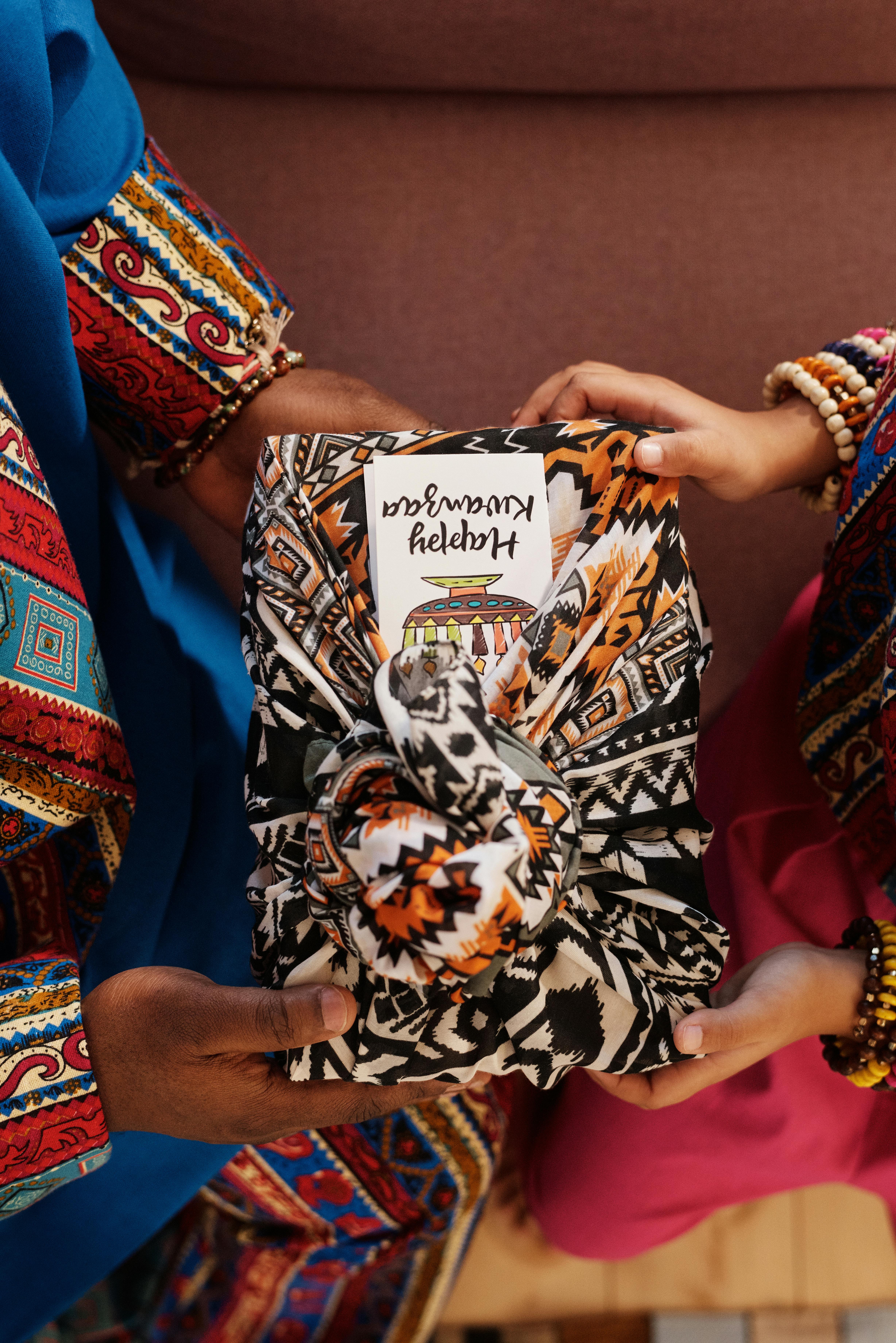 Close-up of hands exchanging a Kwanzaa gift wrapped in traditional fabric.