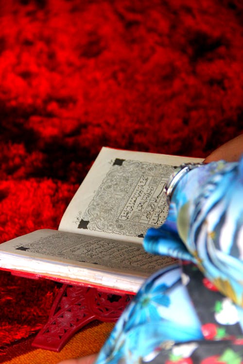 A Person in Blue Floral Clothes Reading a Quran 
