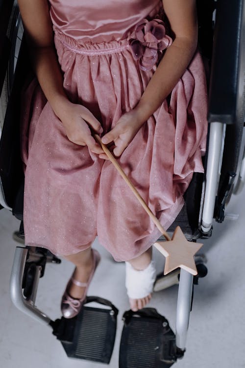 Free A Girl in a Pink Dress Sitting on a Wheelchair Holding a Magic Wand Stock Photo