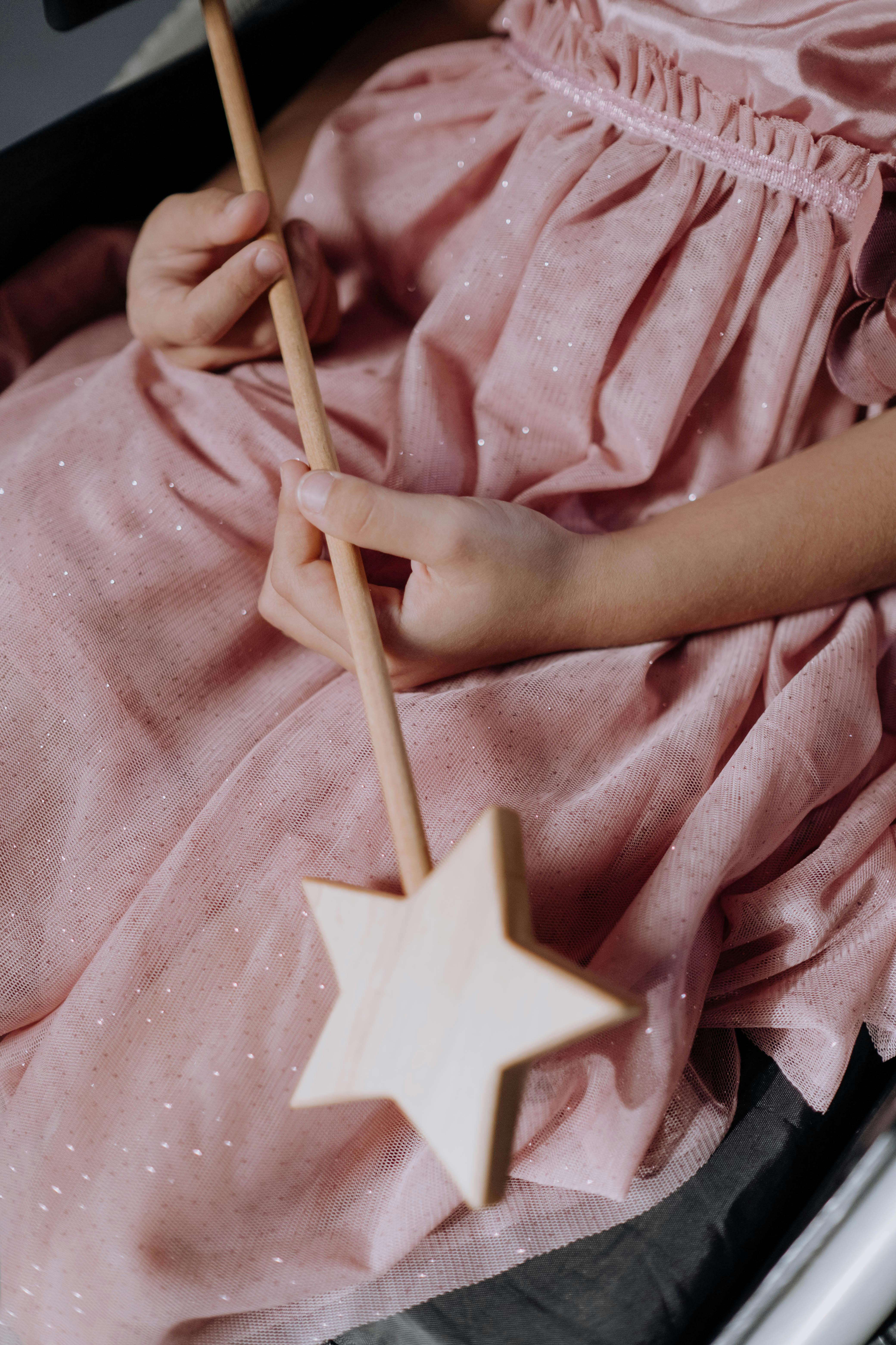 a girl wearing a pink dress holding a magic wand