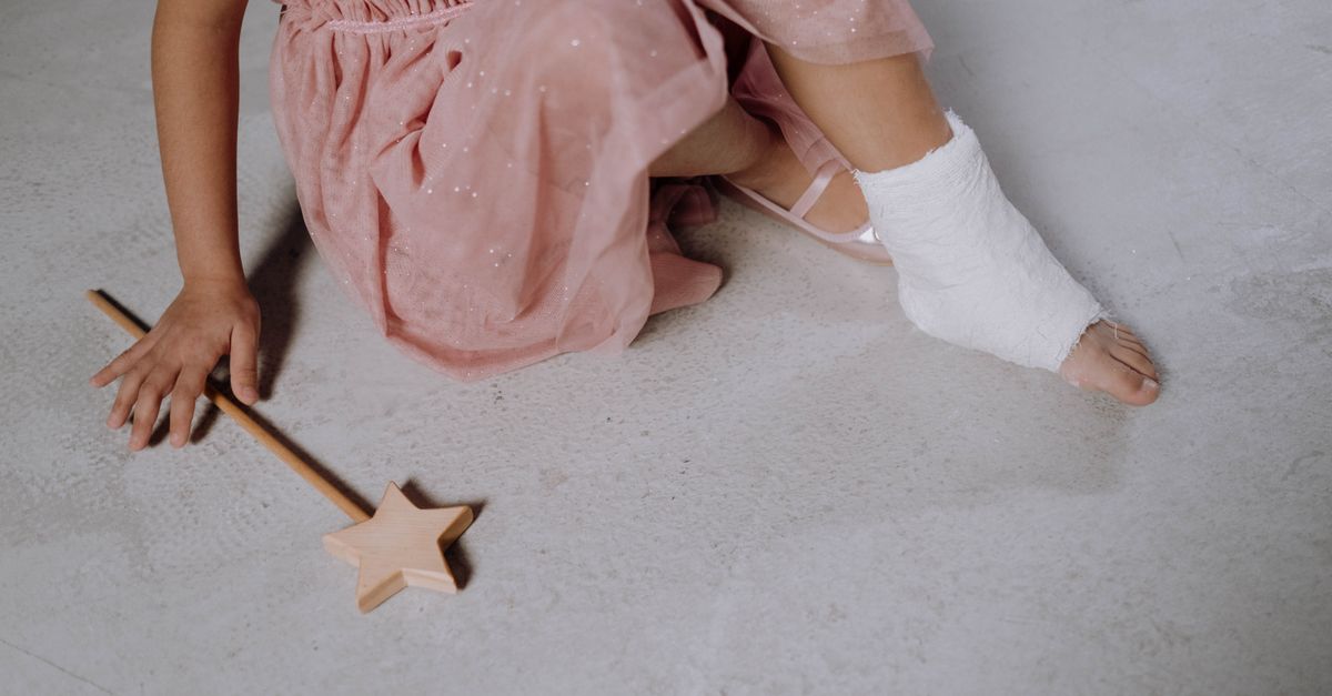 Close-up of a child's injured foot with cast, wearing a pink dress and holding a magic wand.