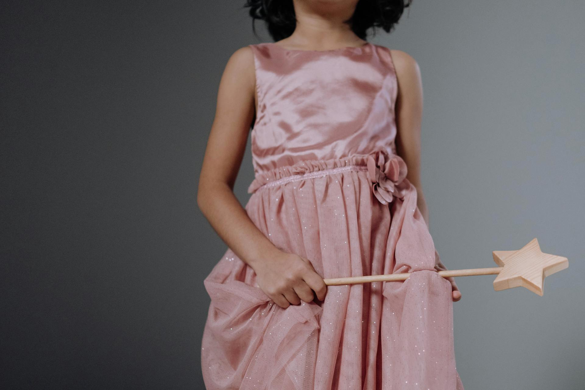 Young girl in pink dress holding a star-shaped wand, embodying a fairytale princess theme.