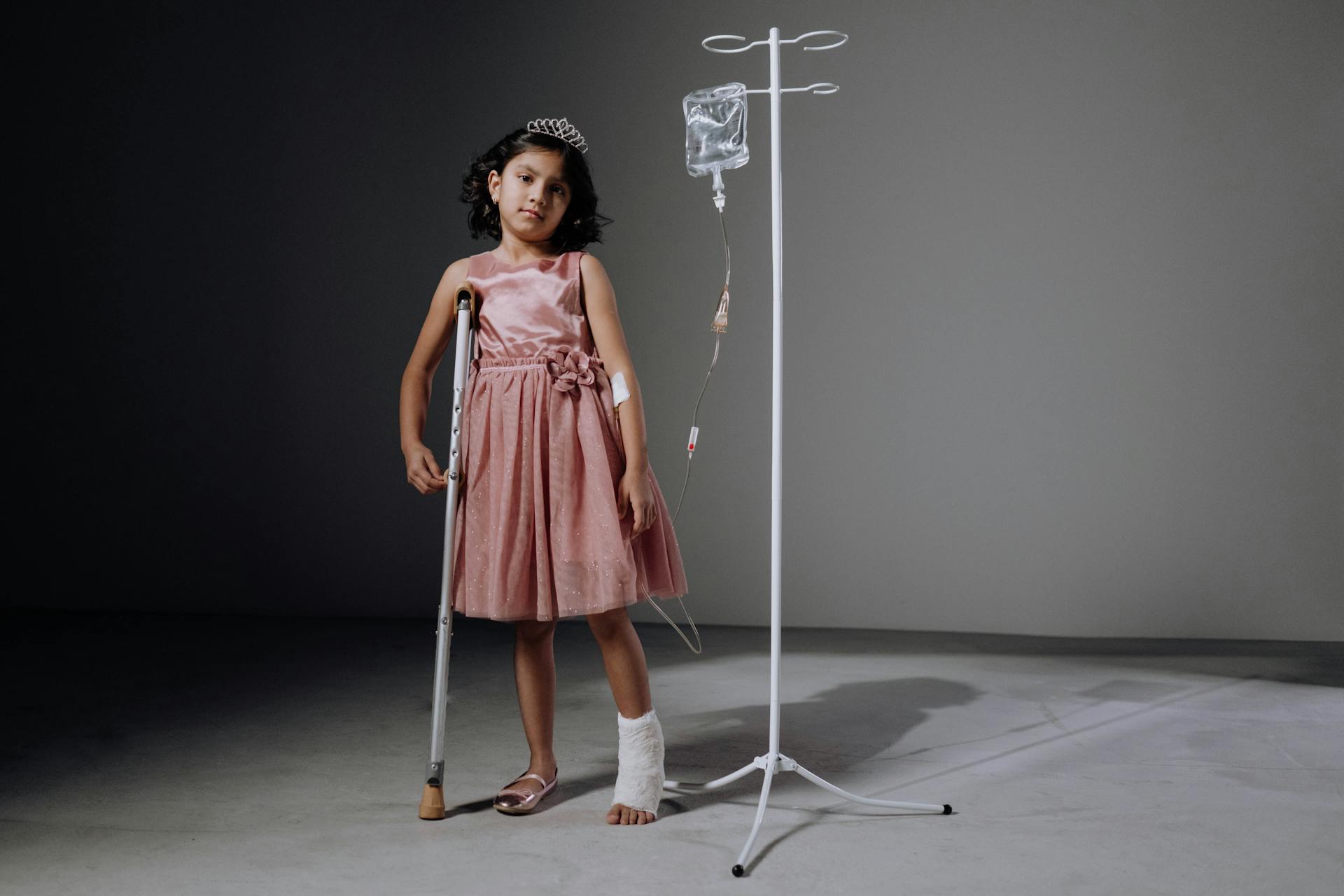 A Girl in a Pink Dress Standing with a Crutch