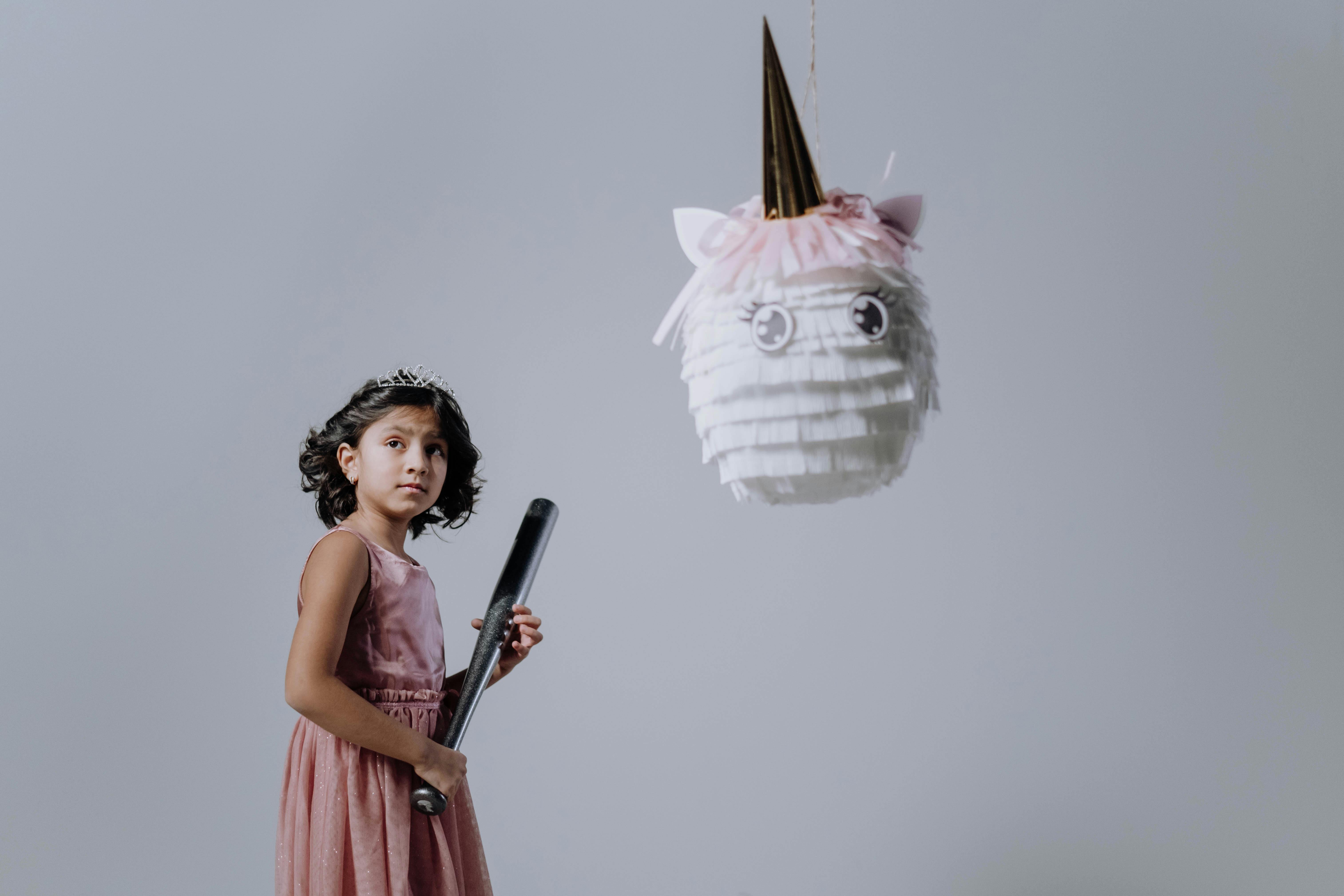 a girl in pink dress standing behind a hanging pinata