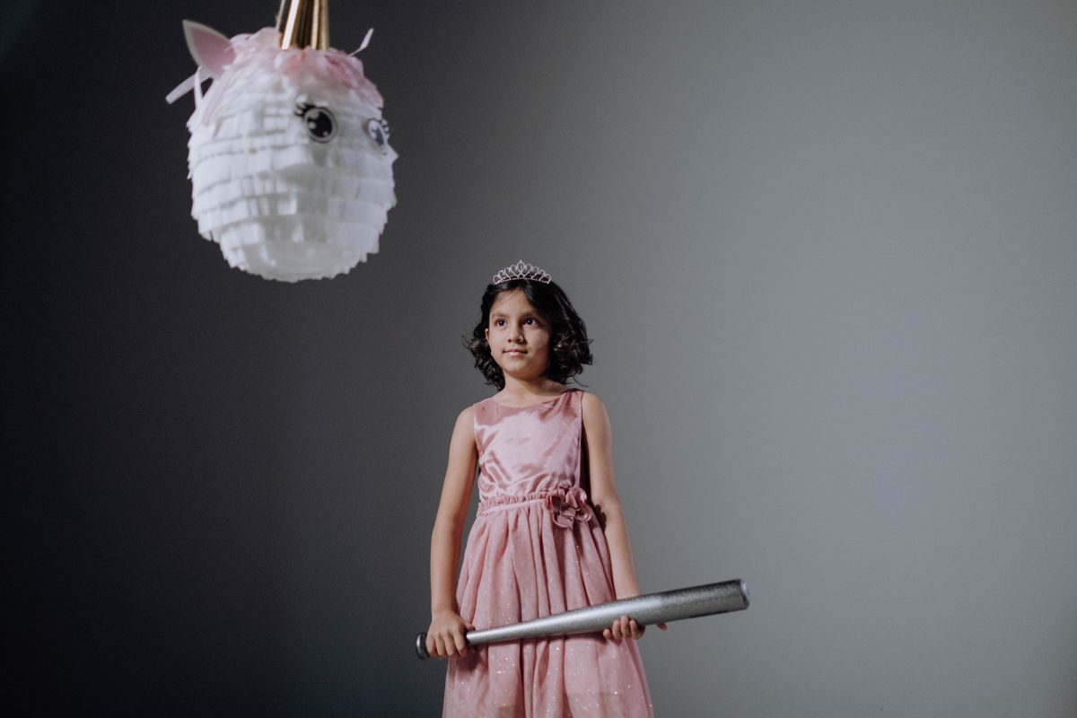 Girl in a pink dress ready to hit a unicorn piñata