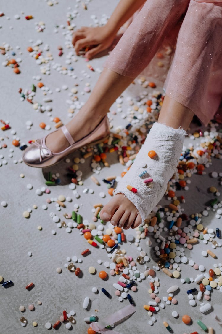 Close-up Of A Child With A Foot In A Cast Sitting Among Scattered Pills 