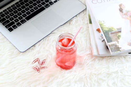 Flat Lay Photo of Glass of Beverage Beside Magazines and Laptop
