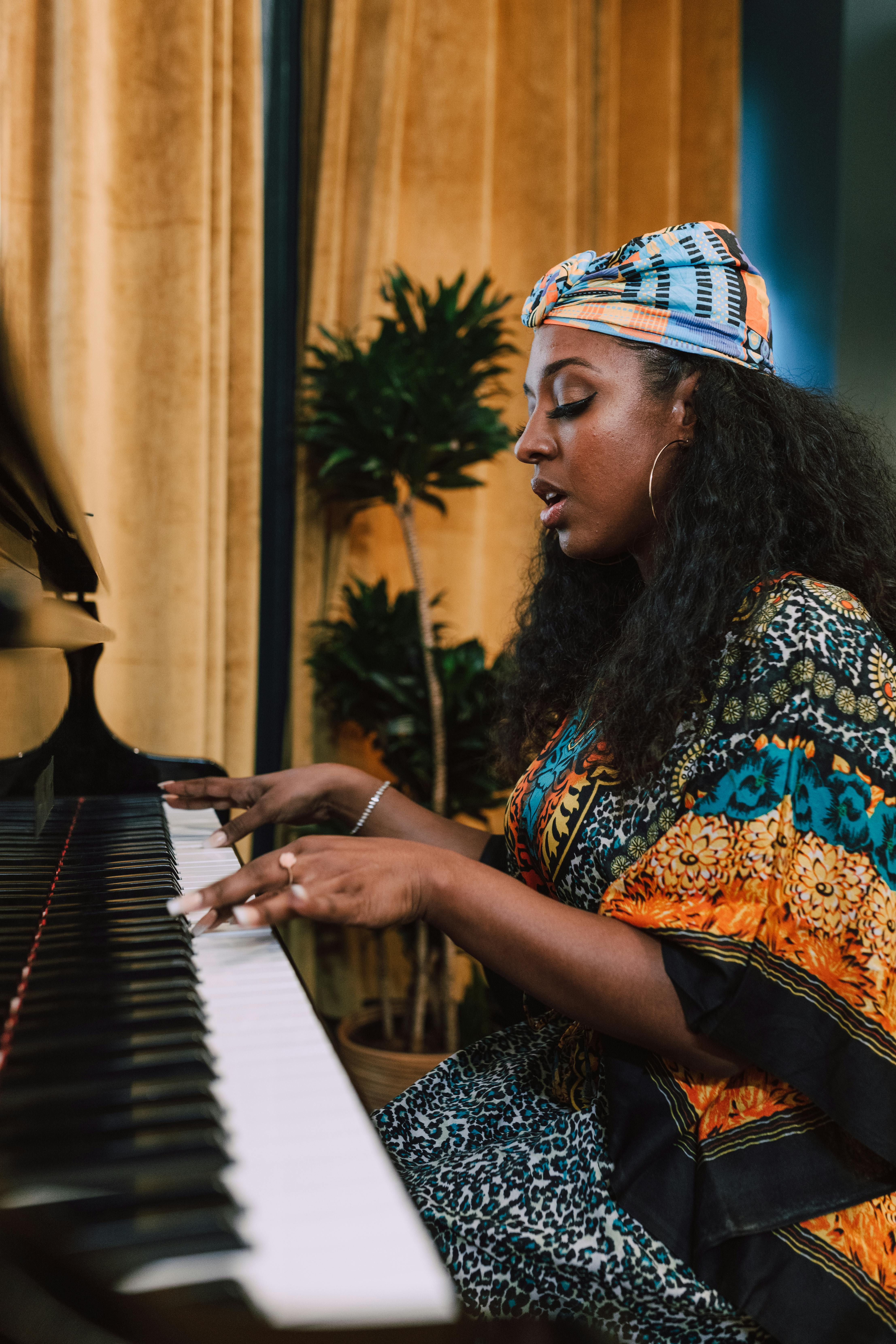 Capivating portrait of an African woman playing piano indoors wearing a vibrant kaftan and headwrap.