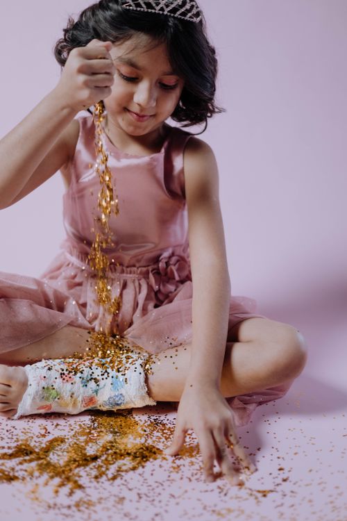 Free A young girl in a pink dress plays with glitter against a pink studio backdrop. Stock Photo