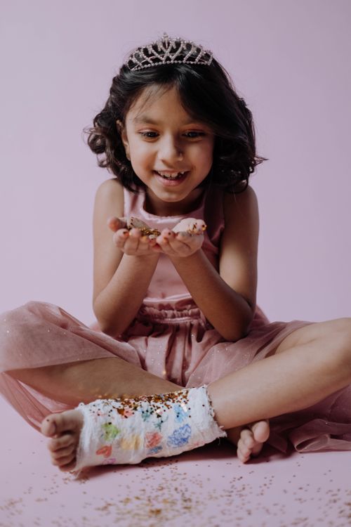 Free Young girl in a pink dress and tiara smiles joyfully holding glitter, showcasing innocence and fun. Stock Photo