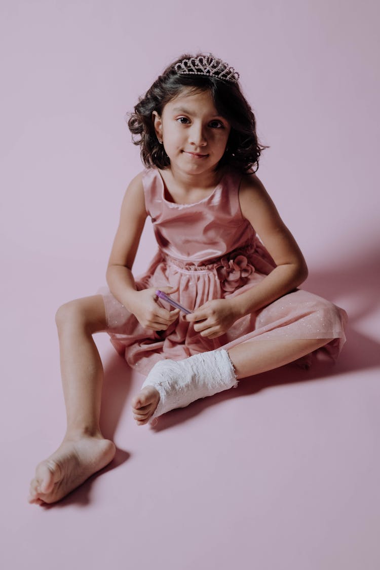 A Girl In A Pink Dress Wearing An Orthopedic Cast