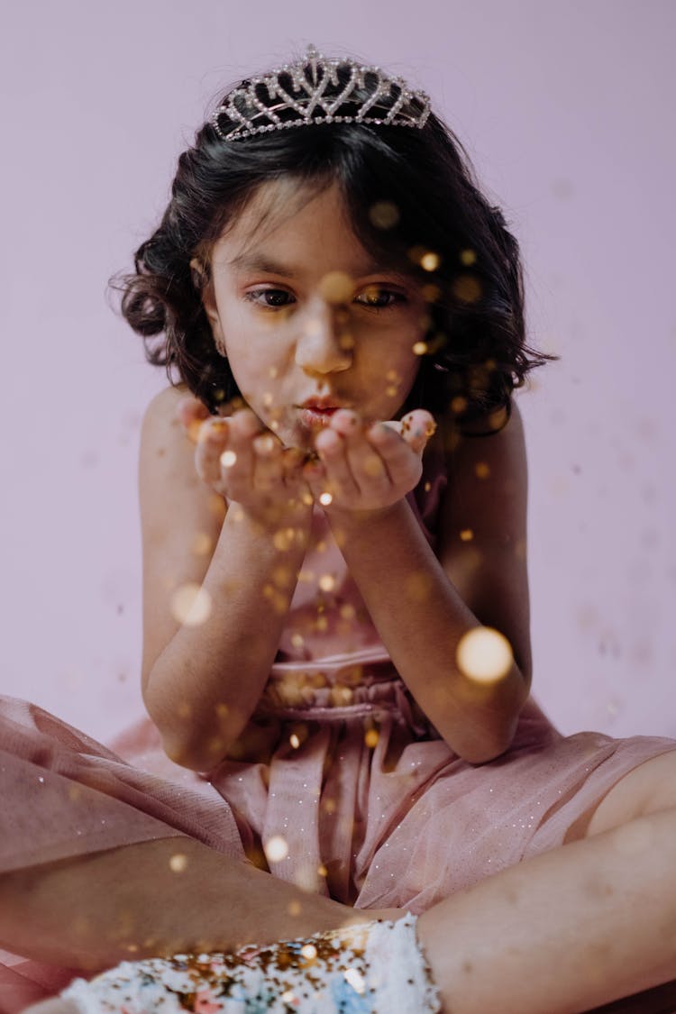 A Girl Wearing A Tiara Blowing Glitters