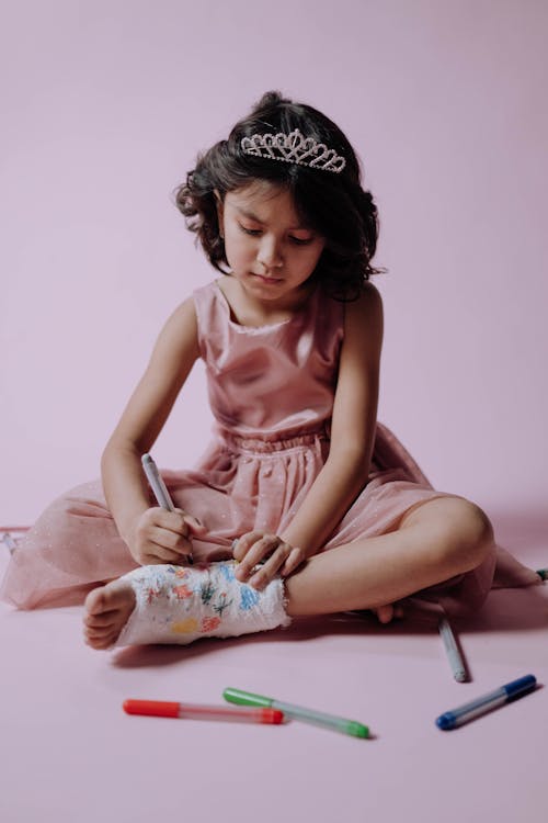 A Pretty Girl in Pink Dress Drawing on Her Orthopedic Cast