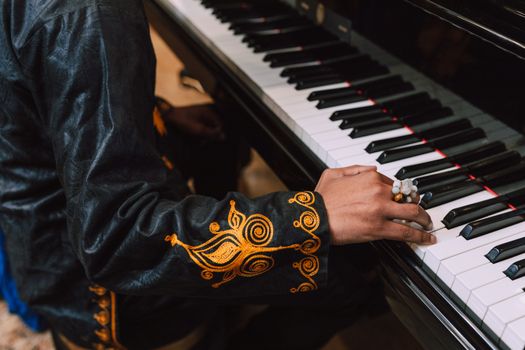 Close-up of a person playing piano, wearing traditional clothing with detailed embroidery.