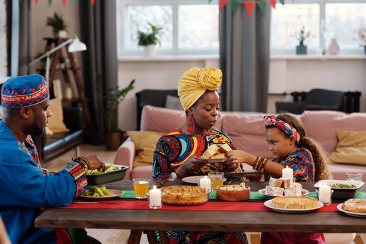 Family enjoying a Kwanzaa celebration with traditional clothing and foods in a cozy home setting.