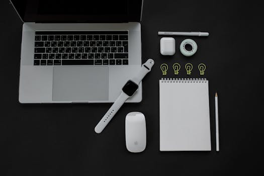 Flatlay of modern gadgets including laptop, smartwatch, and accessories on black surface.