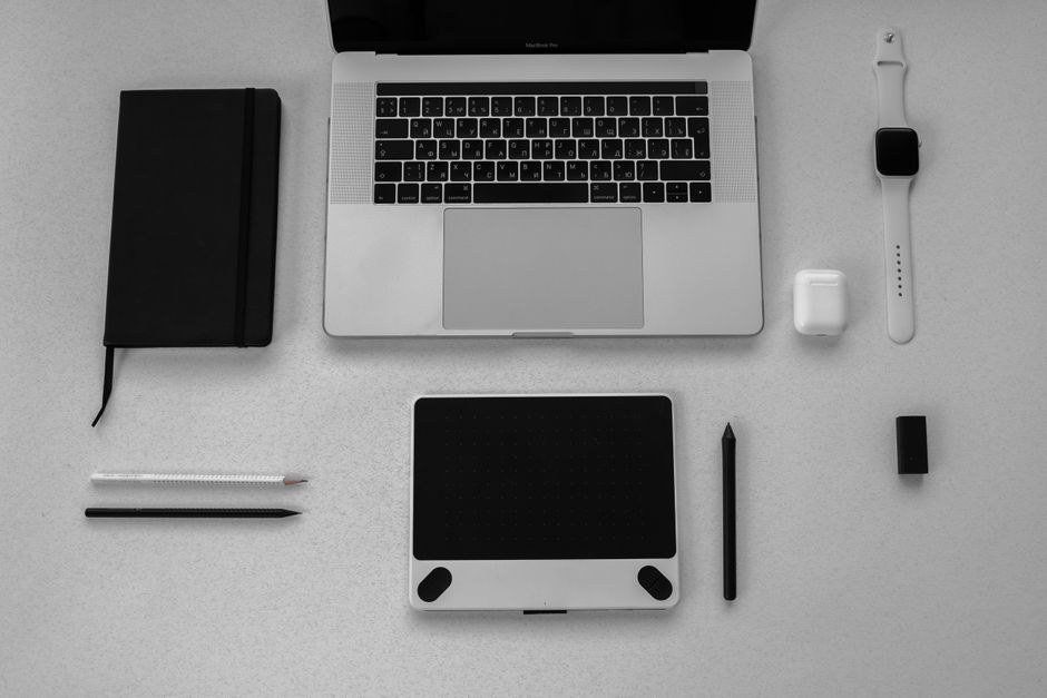 Theragun Pro vs Hypervolt 2 Pro: Deep Tissue Recovery Battle (2024) Black and white flatlay of stylish tech gadgets including laptop and smartwatch on a desk.