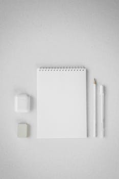 Flat lay of a clean white sketchbook with pencil, eraser, in a minimalist setting.