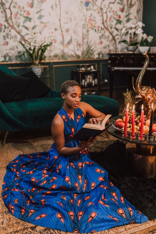 Free Woman in Blue and Orange Dress Reading A Book Near Table Stock Photo