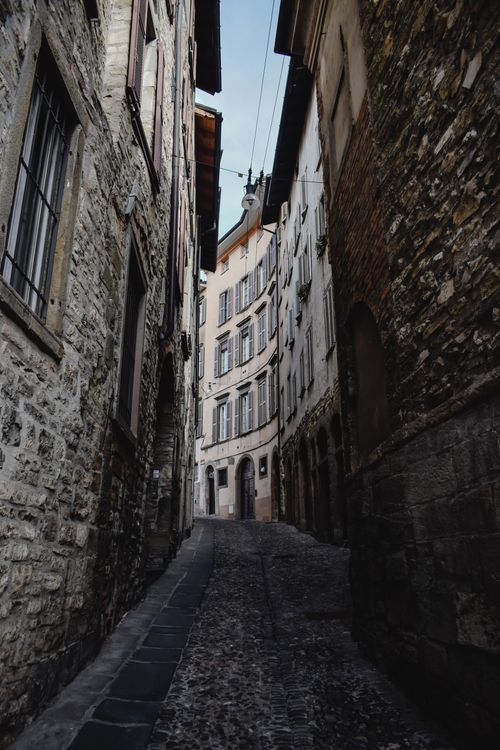 Free Explore a narrow cobblestone street lined with historic stone buildings in Bergamo's old town. Stock Photo