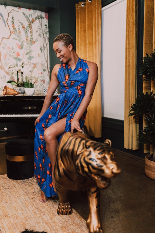 Woman in Blue and Brown Sleeveless Dress Sitting On A Tiger Figurine
