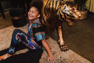 Happy African American girl in colorful traditional attire sitting and laughing indoors with golden tiger statuette.