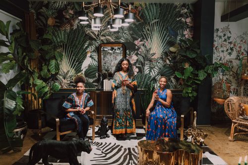 Free Three African women in traditional attire celebrating indoors with vibrant decor Stock Photo