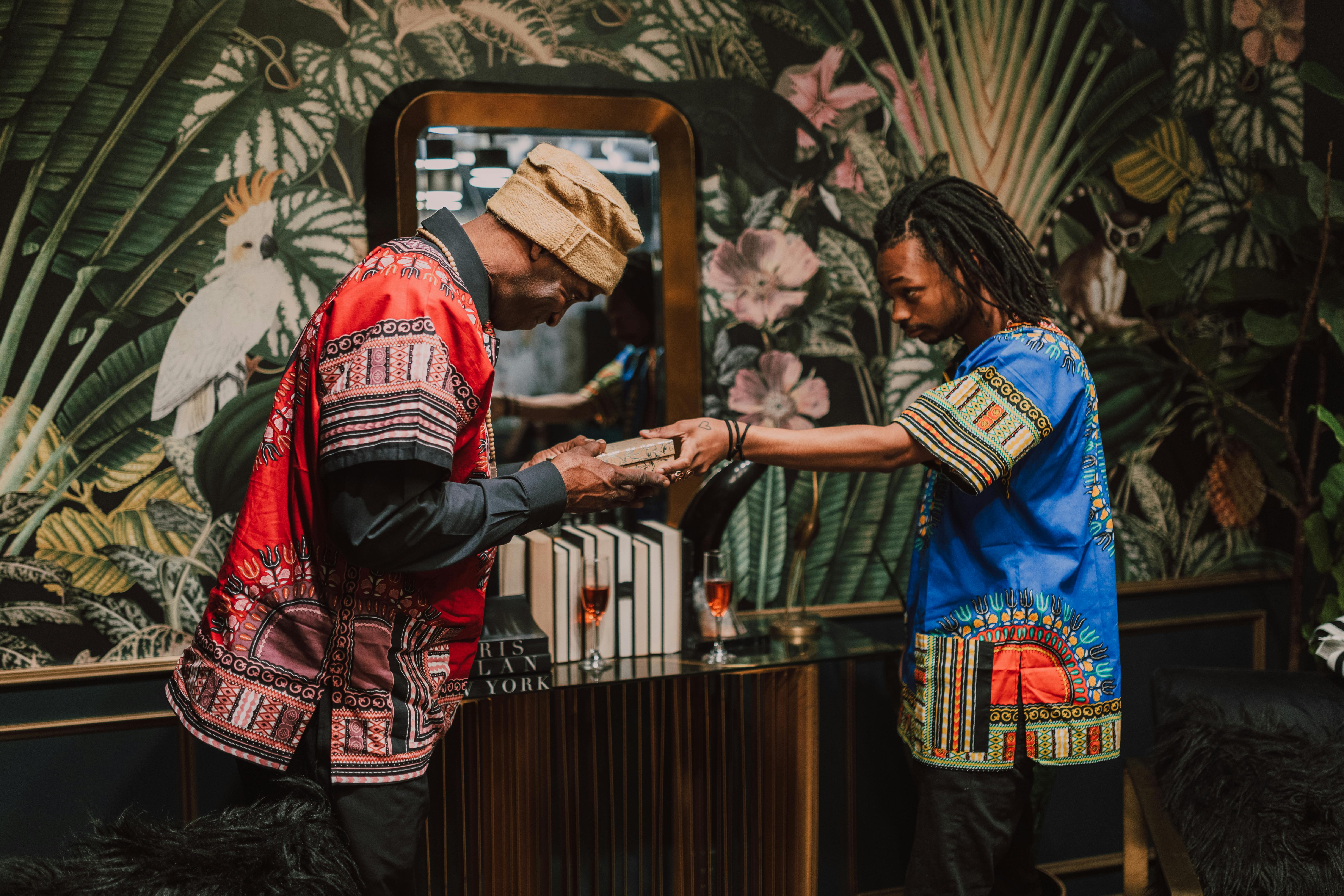 Two men exchange gifts during a Kwanzaa celebration, wearing traditional dashikis.