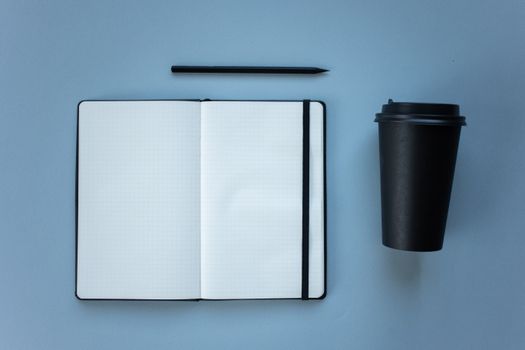 Flat lay of a notebook, pencil, and coffee cup on baby blue background.