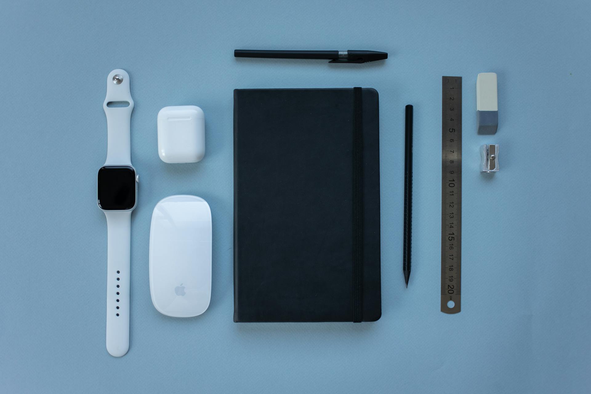 Modern tech gadgets and stationery arranged on a soft blue background in a flat lay style.