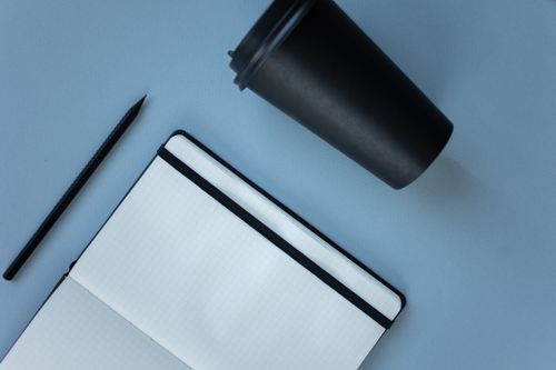 Free Simple composition of a notebook, pen, and disposable cup on a blue background, creating a minimalist feel. Stock Photo