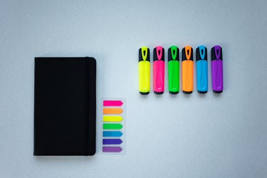 Flat lay of vibrant markers and a black notebook on a light background, perfect for office use.