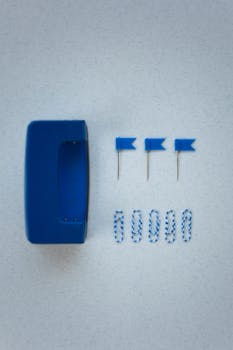 Neatly arranged blue office supplies include a hole puncher, paper clips, and push pins on a textured surface.