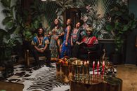 Group celebrating Kwanzaa with traditional clothes and candles indoors.