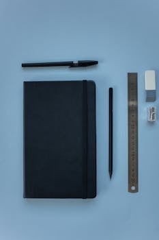 A neatly arranged flat lay of office supplies on a blue surface, featuring a pen, notebook, ruler, and more.