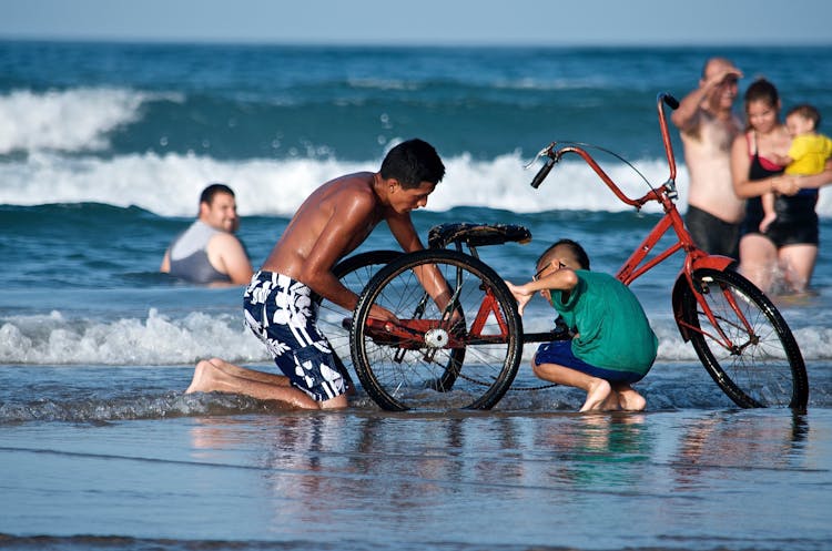 Man And Child Fixing A Bicycle On The Beach