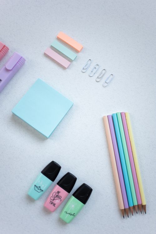 Free Flat lay of pastel stationery items including pencils, paper clips, and sticky notes on white surface. Stock Photo