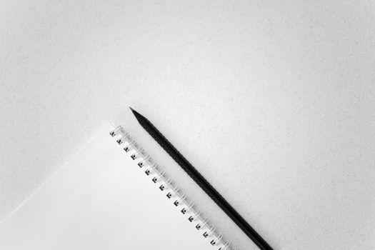 A spiral notebook and black pencil arranged on a plain white background, offering ample copy space.
